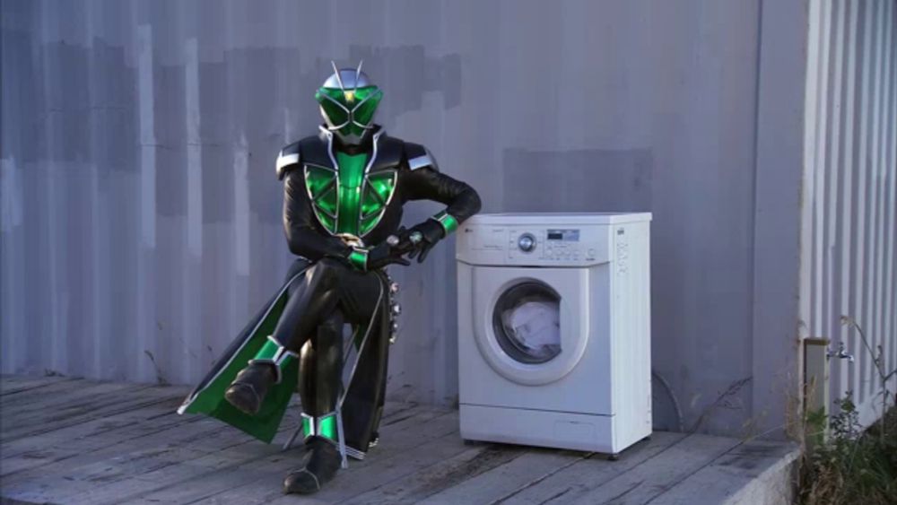 a man in a superhero costume sits next to a washing machine