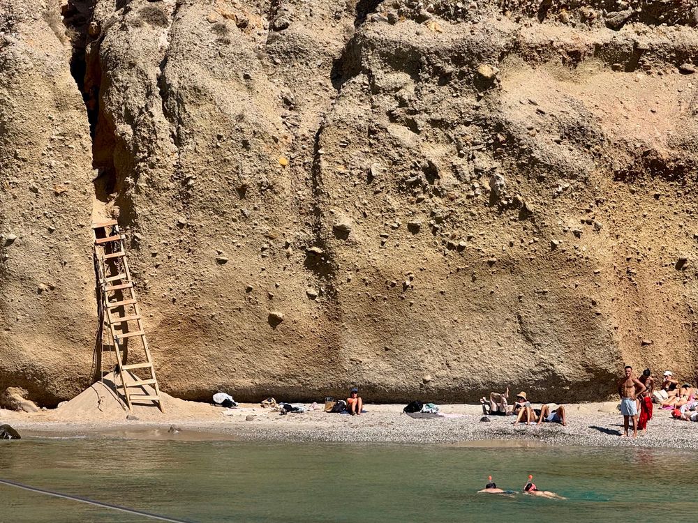 A beach on the island of Milos in Greece. Best accessed by boat as the ladder (left) is extremely rickety. Cliffs, beach, water, tiny little people. Big ladder.
