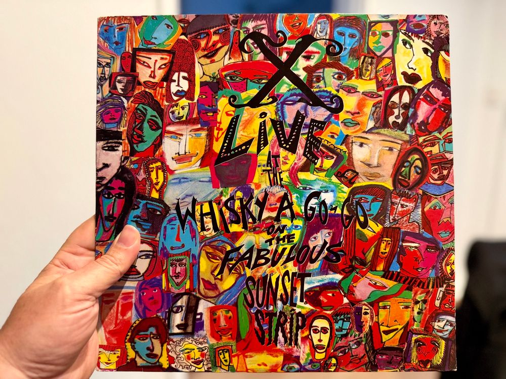 Me holding my newly purchased copy of the LP “X Live at the Whisky A Go-Go on the Fabulous Sunset Strip”. The cover is a collage of colourful hand drawn faces.