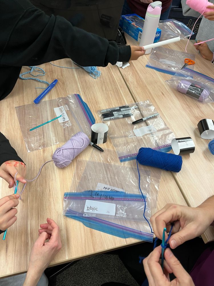 A photo of hands and crochet hooks and balls of yarn and plastic Ziploc bags to store their projects in…