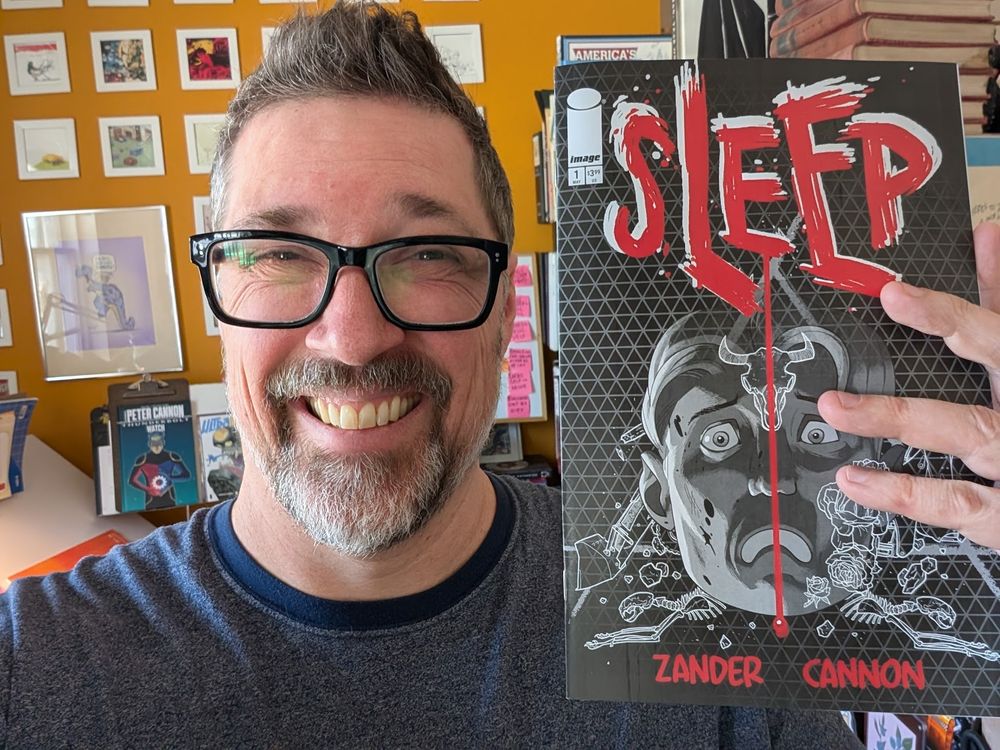 A photo of a smiling middle aged cartoonist (Minneapolis' own Zander Cannon) holding up his latest comic book: Sleep #1, published by Image Comics.