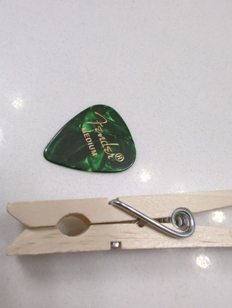 A clothespin and an emerald green Fender medium guitar pick