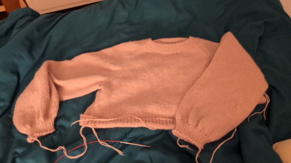 A finished (!!) pink knitted sweater is lying on a blue blanket. Well ignore the loose ends of yarn that will have to be woven in eventually (but today is not the day).