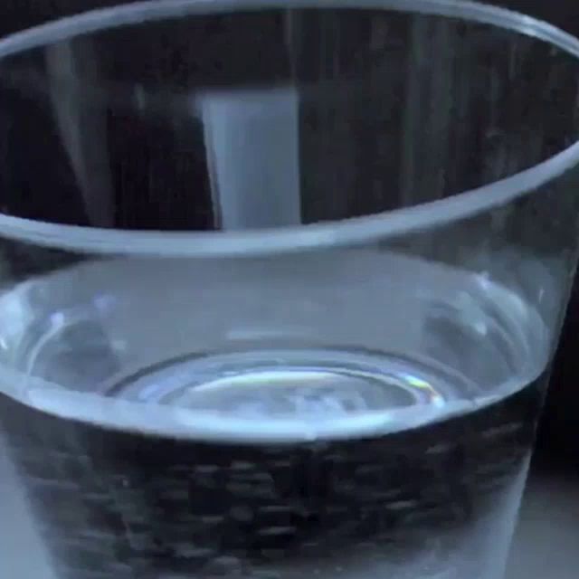 a glass of water is sitting on a table in front of a black background