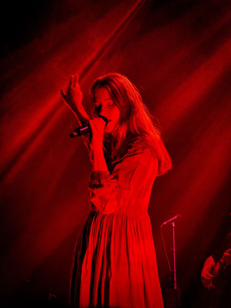 Photograph of Paris Paloma in concert, at The Opera House, Toronto, March 13th, 2025.  The singer is pictured holding a microphone, bathed in a red glow.