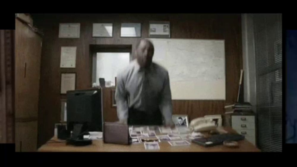 a man is standing in front of a desk with a computer and a phone