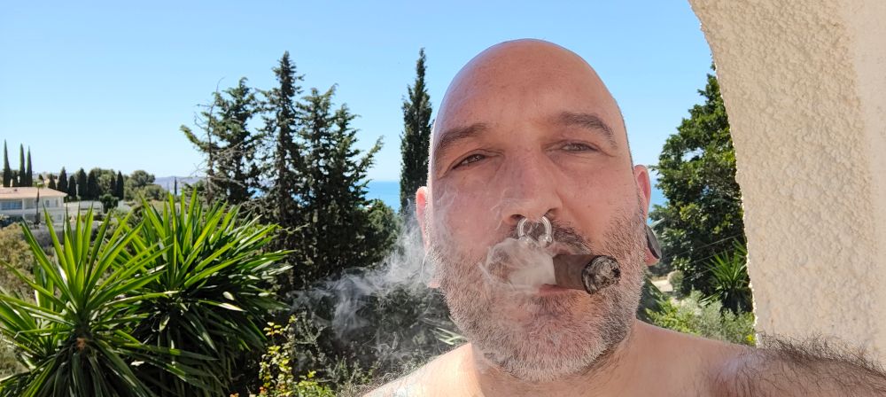 Cigar smoking man with septum, Mediterranean sea in the backgrond
