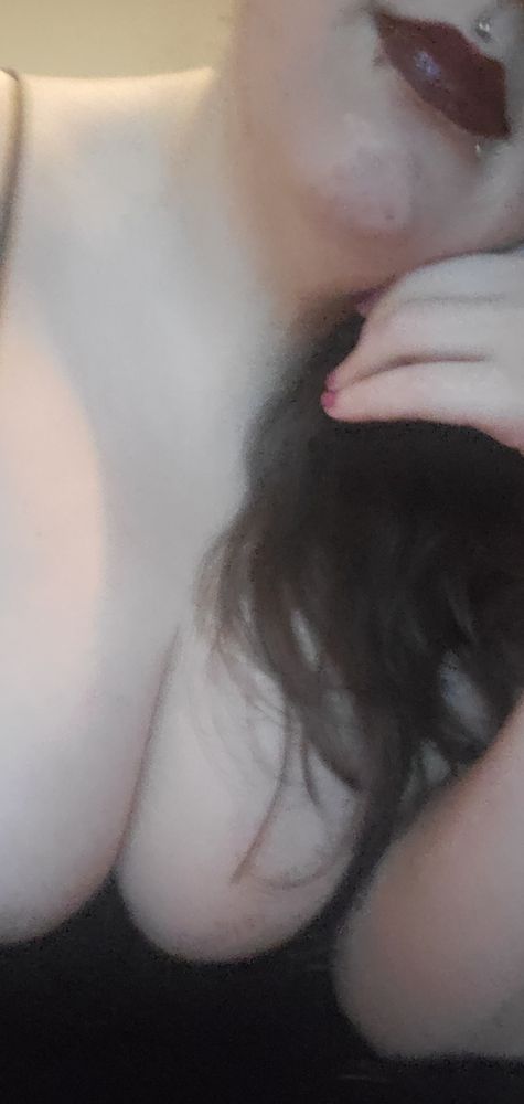 Bratty_Prince showing off his tits, lipstick/lip gloss, and nails. Their nails are painted a pinkish purple with some blue sparkles and their lips are a dark red with glitter gloss. Their lips are tilted into a sadistic grin