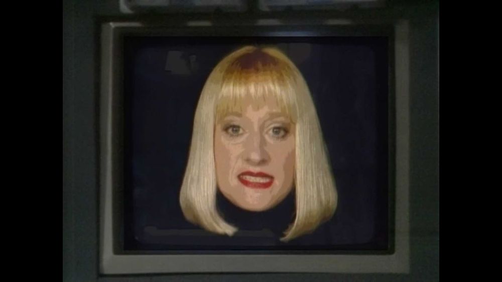 The user interface for the Holly computer on Red Dwarf, depicted as the head of a blonde woman with a shoulder length bob cut on a black background 