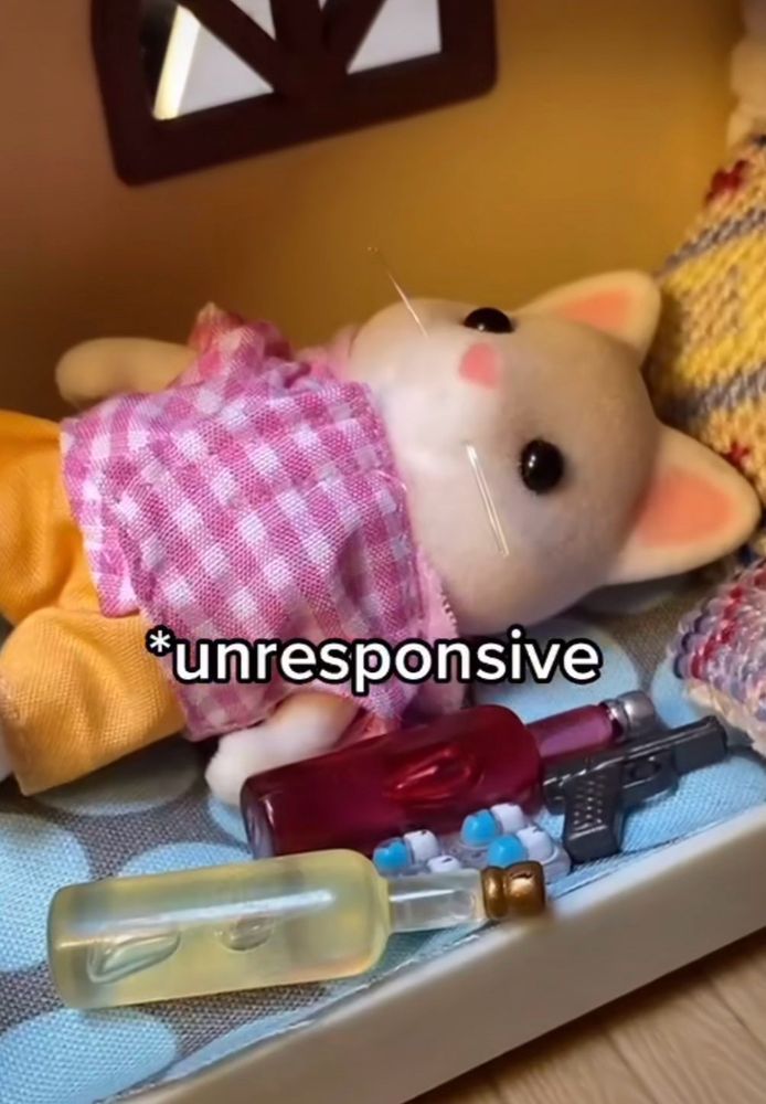 A silly meme of a stuffed mouse toy laying on its back, with miniature pills, bottles, and a gun next to it with the caption “Unresponsive.”