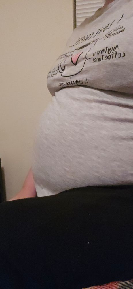 A wild trans woman with a round, protruding belly nestled in her lap