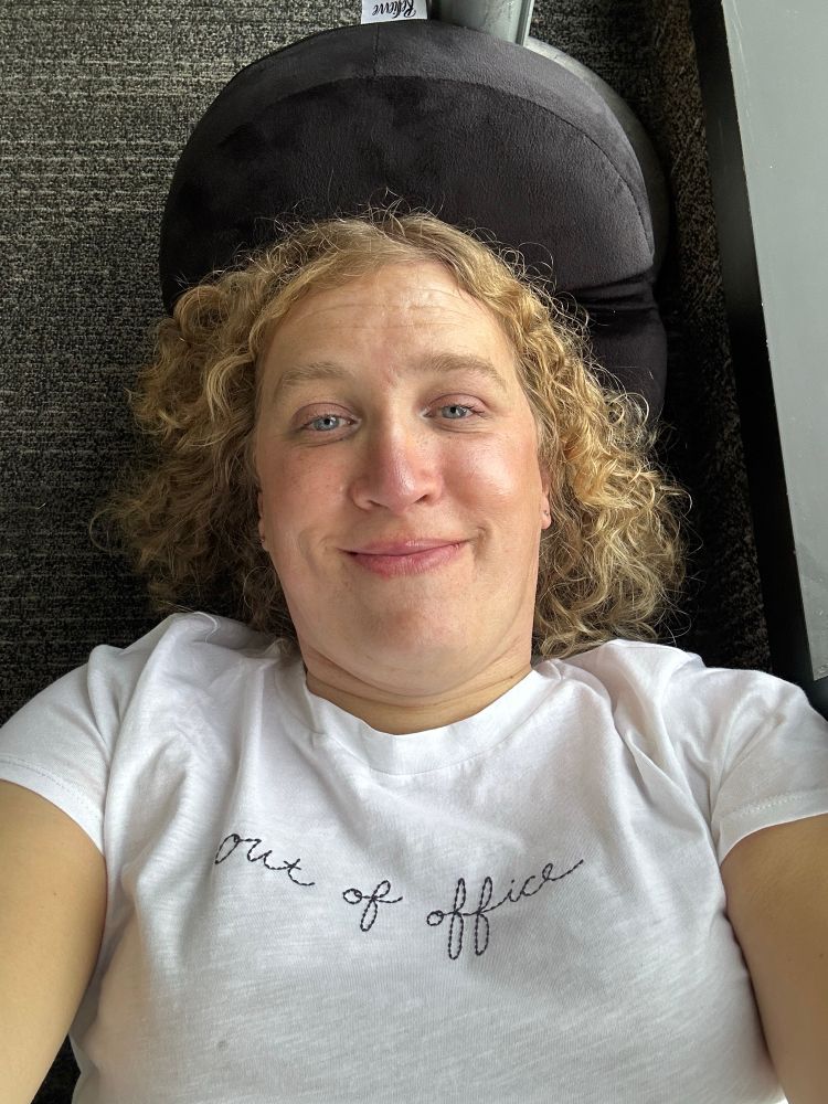 Woman laying on the floor of an airport. Her expression is half smile/ half pain