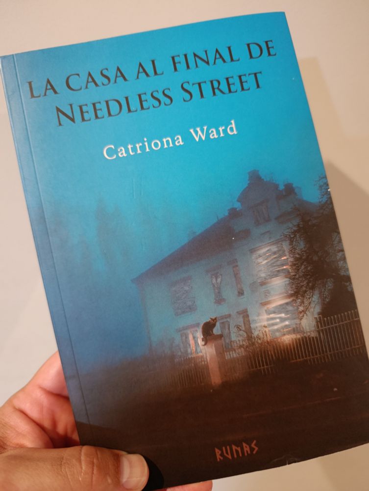 Portada de la novela La casa al final de Needless Street de Catriona Ward.
Una casa en ruinas iluminada por dentro sobre el fondo azul y nublado de un bosque
