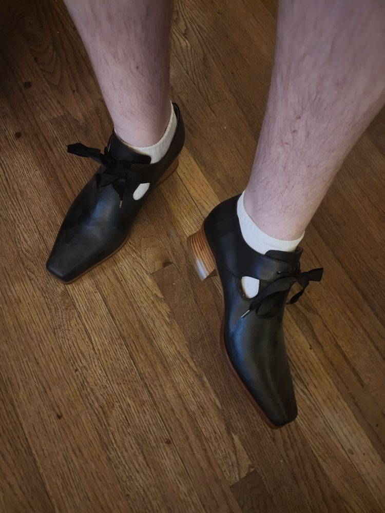My legs, feet in a pair of wooden-heeled leather shoes that are replicas of a square-toed style popular in the 1700s 