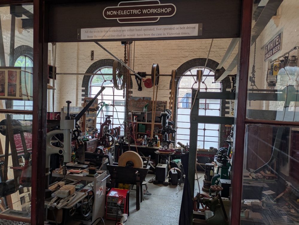 The non-electric workshop. The sign says "all tools in this workshop are other hand operated, foot operated, or belt driven from the overhead line-shaft as would have been the case in Victorian times."