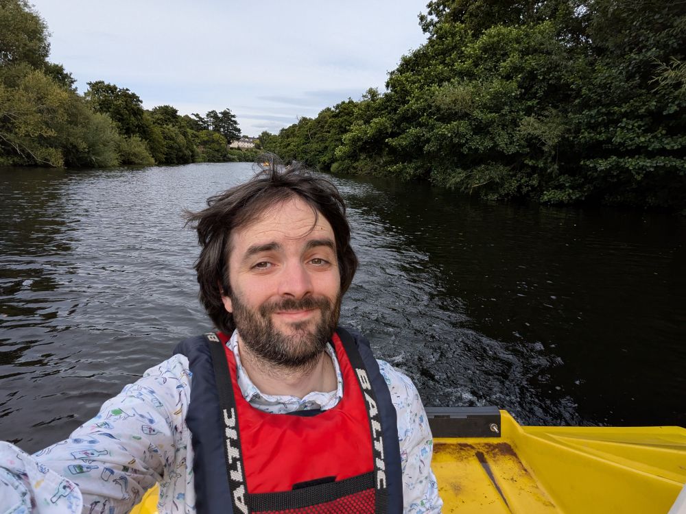 Selfie on a pedalo on the River Usk, wooded on either side as the river stretches behind me