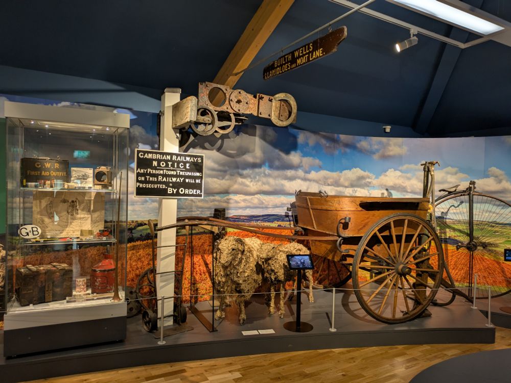 One of the displays in the museum: a carriage, a penny farthing bike, a railway signal, an artwork of some sheep, a display case of rail paraphernalia