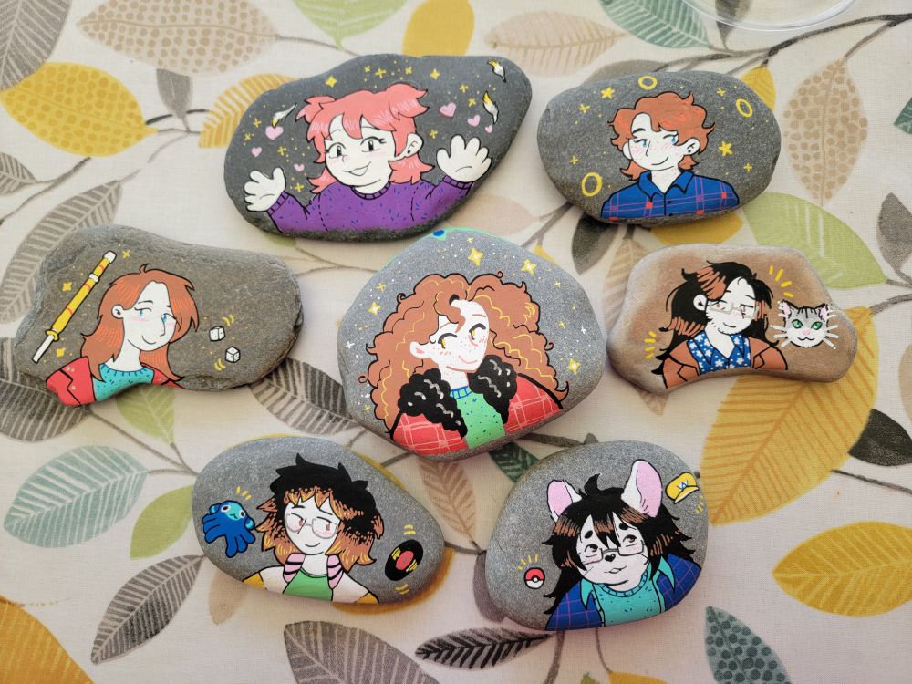 six hand-sized rocks all painted with individual people on each one. 