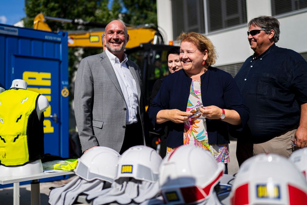 Bundesministerin Korinna Schumann hält eine Schutzbrille in der Hand, Josef Muchitsch, Bundesvorsitzender der Gewerkschaft BAU-HOLZ und der PORR-Betriebsratsvorsitzende stehen neben ihr. 

© BKA/Schrötter 