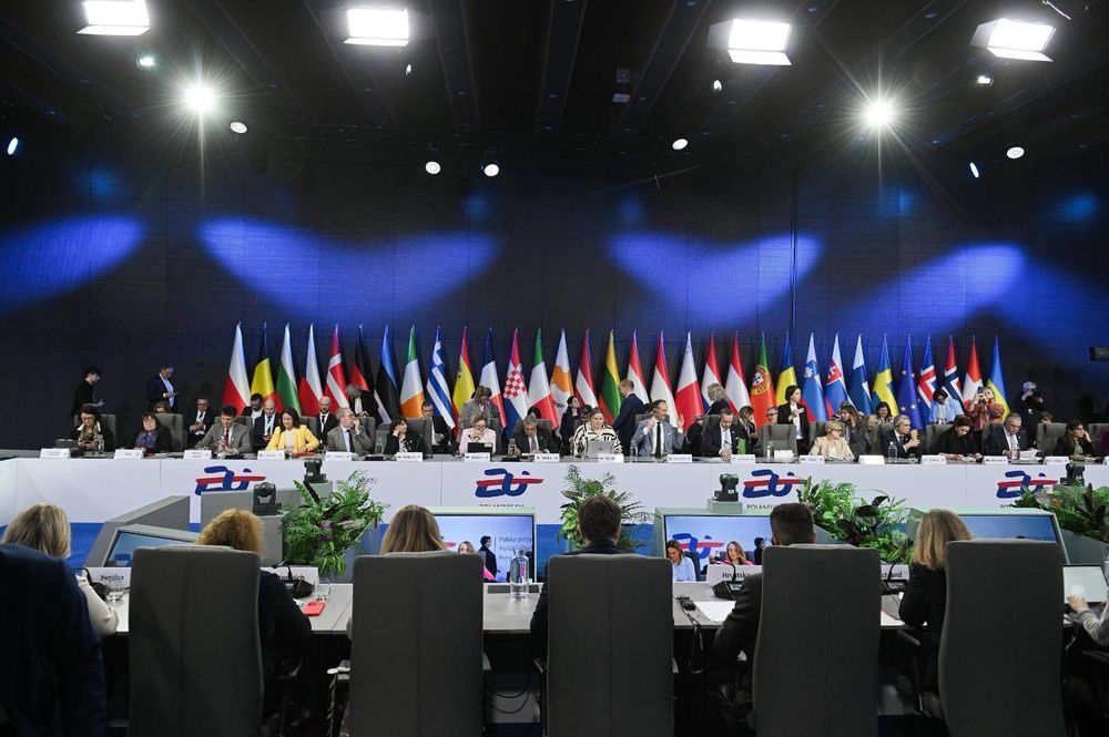 Eine Gruppe von Menschen sitzt sich an einem sehr langen, ovalen Tisch gegenüber. Im Hintergrund sind Länder-Flaggen zu sehen.

© The Chancellery of the Prime Minister/PAP S.A.