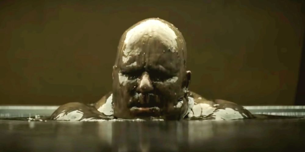 kuvakaappaus elokuvasta Dyyni, isokokoinen kalju mies nousee mustan öljyn seasta