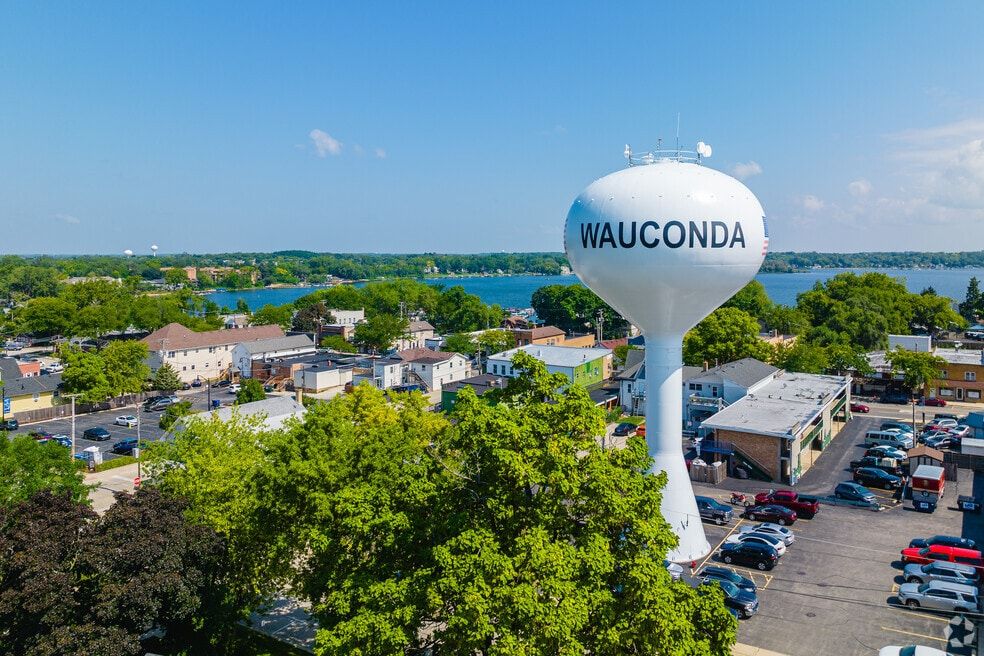 An idyllic aerial view of a water tower overlooking the treeline and buildings of a small midwestern village near a lake. The village in Wauconda, Illinois