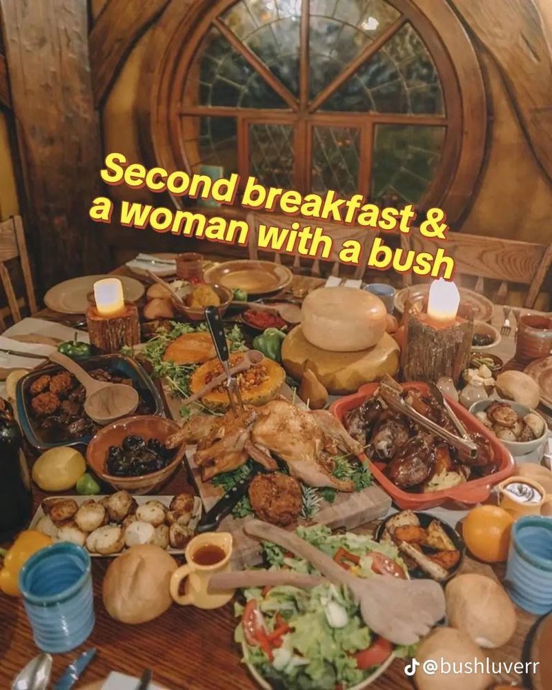 A lavish breakfast spread of foods on a large dining table with the caption: ’Second breakfast & a woman with a bush’