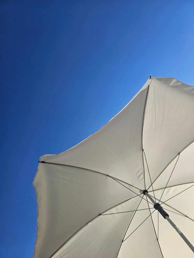 Blick in den blauen Himmel, und in den fast weißen, aufgespannten Sonnenschirm