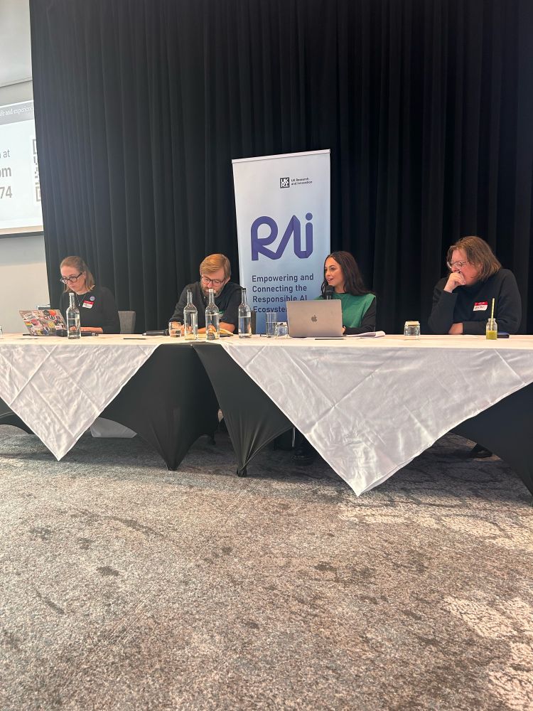 Four people sitting behind a table with a banner that says RAI behind them 