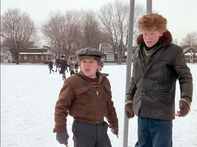 Scut Farkus and his minion from A Christmas Story movie standing next to a pole in the snow looking as tough as they can be.