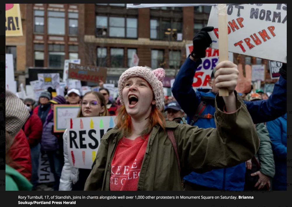 Image of yelling teen holding a sign aloft with crowd of protesters in the background.