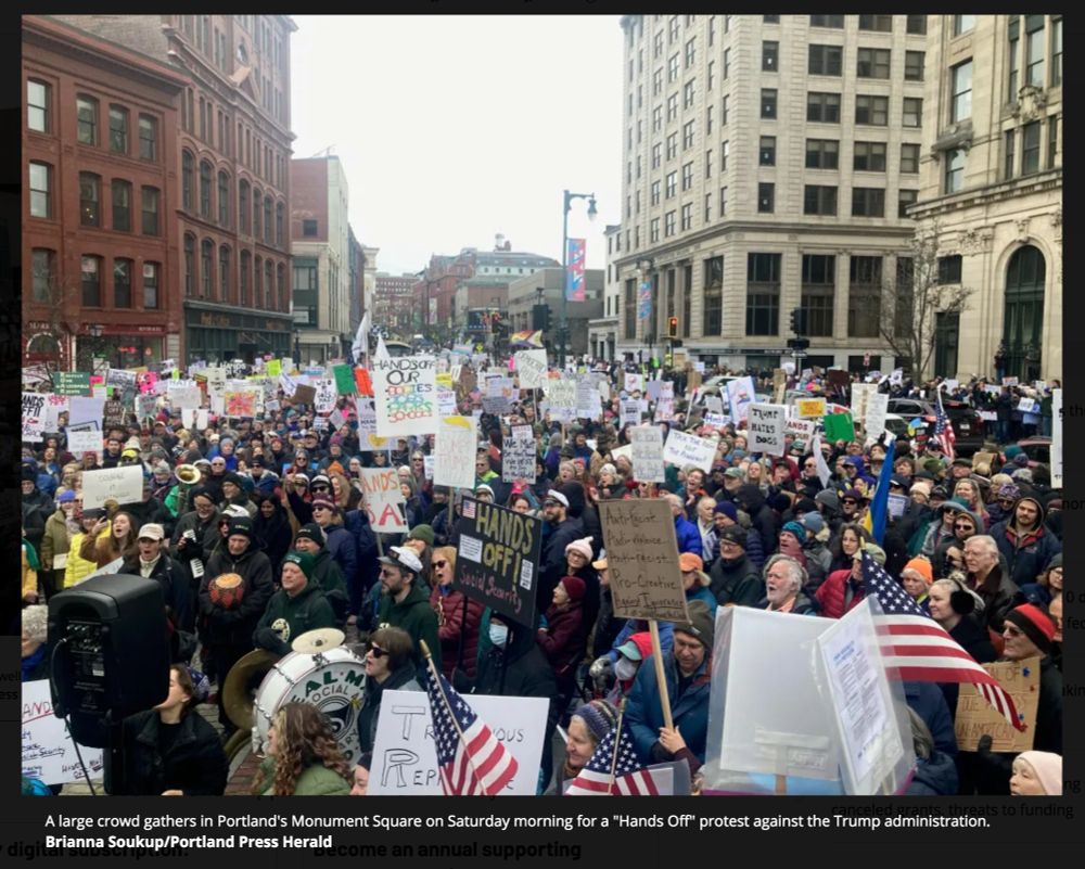 Image of large crowd gathered in protest, stretching into the distance between two rows of tall buildings.