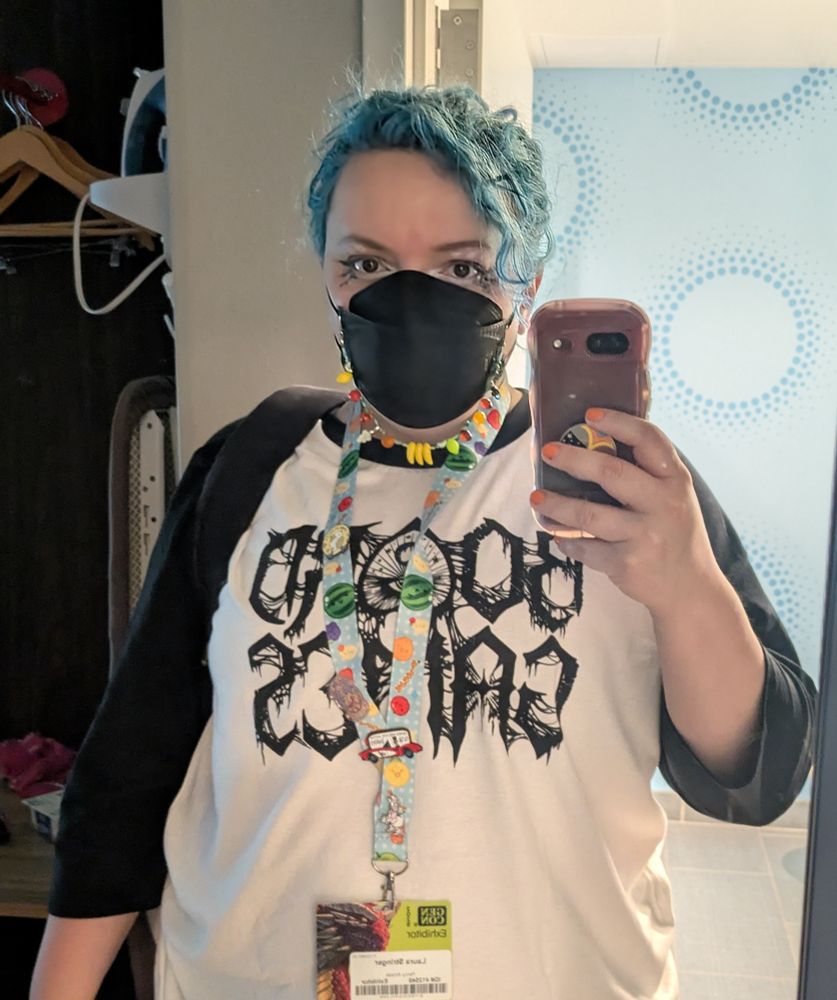Author doing a mirror selfie with metal BOARD GAMES raglan shirt and gothy makeup as well as a fruit motif lanyard and mask chain 