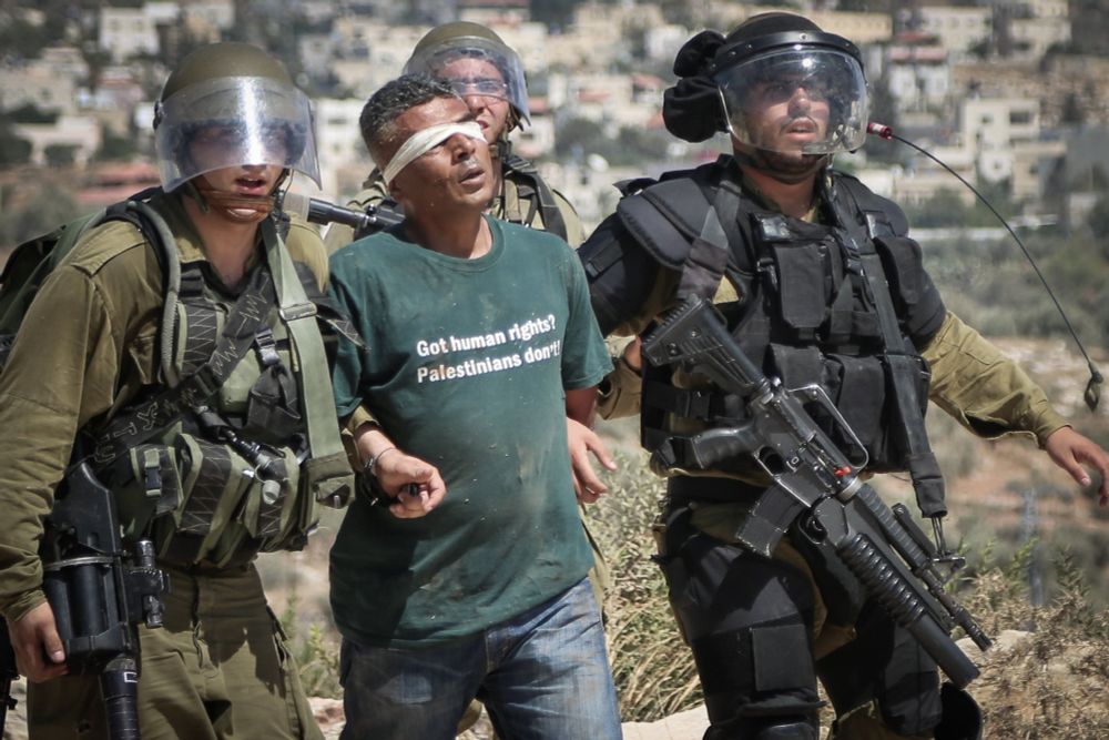 Activist Iyad Burnat being arrested by IDF soldiers while wearing a blindfold and a t-shirt that said "Got human rights? Palestinians don't"
