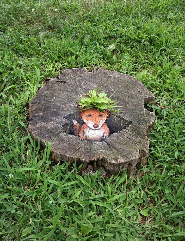 sidewalk chalk drawing of a small fox emerging from a hole "wearing" a tuft of green weeds that are growing out of the stump on which the artwork was drawn.