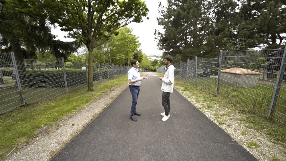 Simon Tschannett und Matthias Lang stehen auf einem asphaltierten Weg zwischen zwei Friedhöfen