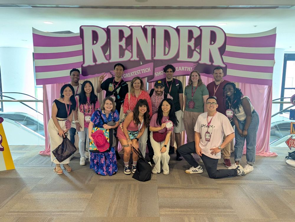 14 men and women posing in front of a horizontal cardboard photography booth with curtains below it with escalators behind it
