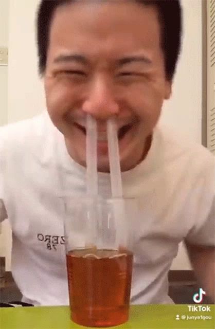 a man is drinking from a glass with two straws sticking out of his nose