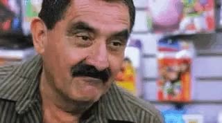 a man with a mustache is making a funny face in front of a shelf of magazines .