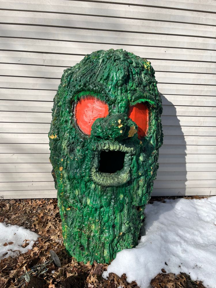 A large sculpture of a textured green monster head big read eyes 