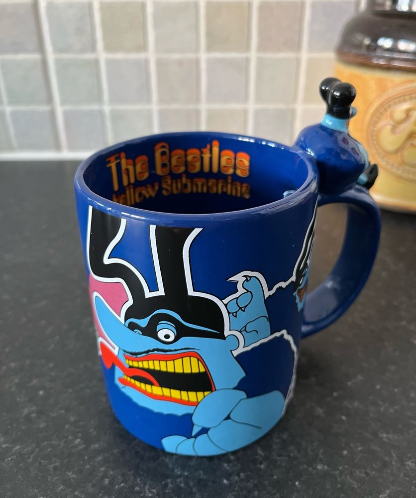 A blue Beatles Yellow Submarine mug emblazoned with Blue Meanie characters from the film. A small 3D Blue Meanie figure sits on the handle 