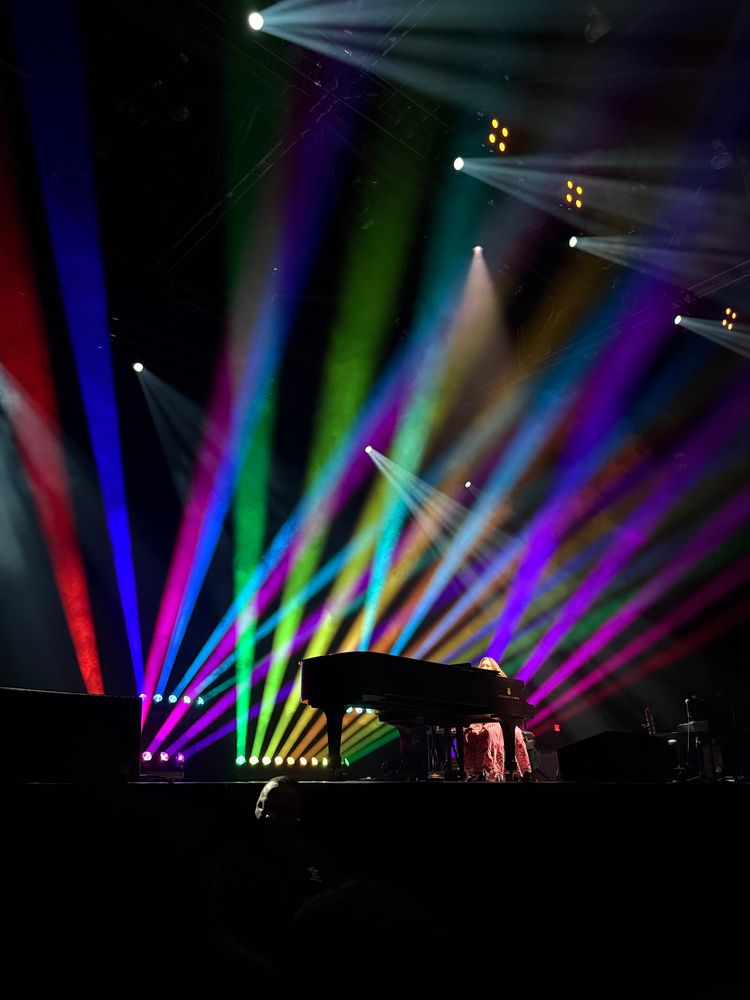 Regina Spektor at her piano, surrounded by Rainbow lights on stage.