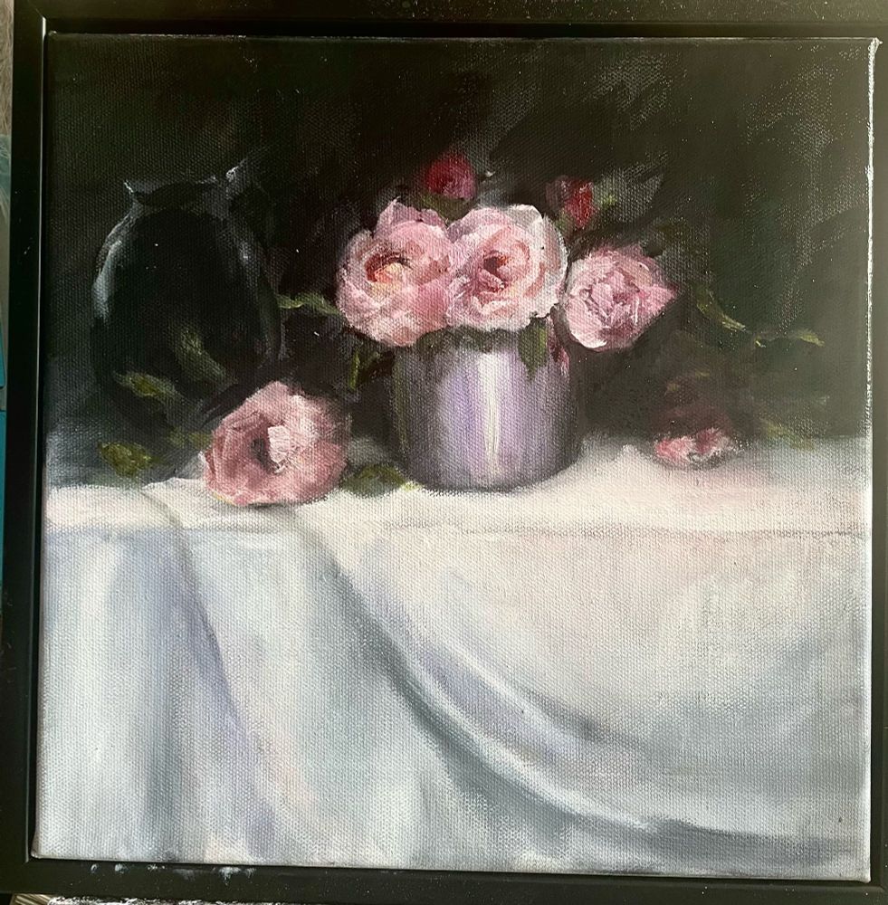 Peonies on a white table with leaves and a glass jug in the shadows 