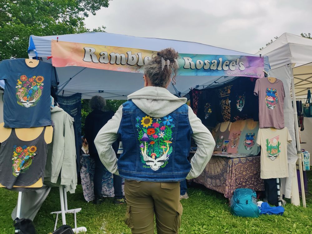 Posterior shot of a woman wearing a hybrid denim/hoodie jacket that has beautiful hand painted Grateful Dead stealie on the back
