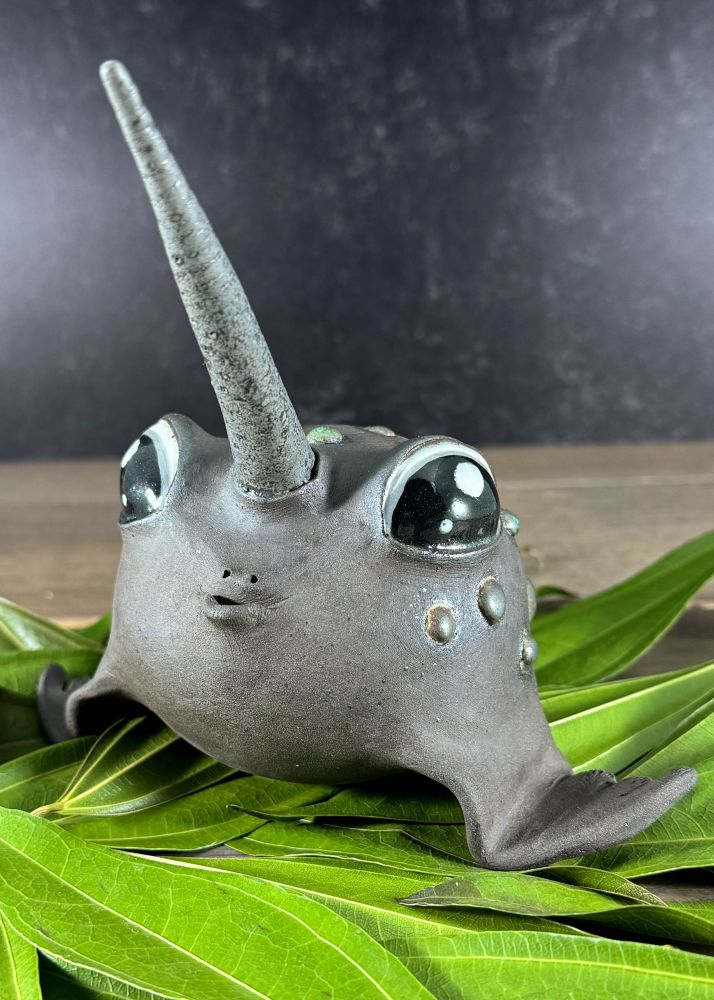 A mythical animal sculpture sits on a bed of leaves. It has big sweet eyes, a fish mouth, a narwhal horn, seal fins, toad spots, and a beaver tail all in dark clay. 

Meeble is an adult female rare Narwhal-Toad/Seal-Beaver mix up for adoption. She really loves kisses and will purse her fishy underbite for you day and night. However, she has no idea where her horn is most of the time and should always be supervised around small children and other animals. Meeble has been known to steal household items and use them to dam doorways, but her dams are artistic and comfortable, to be enjoyed by all. Adoption fee $245 plus transport costs. 