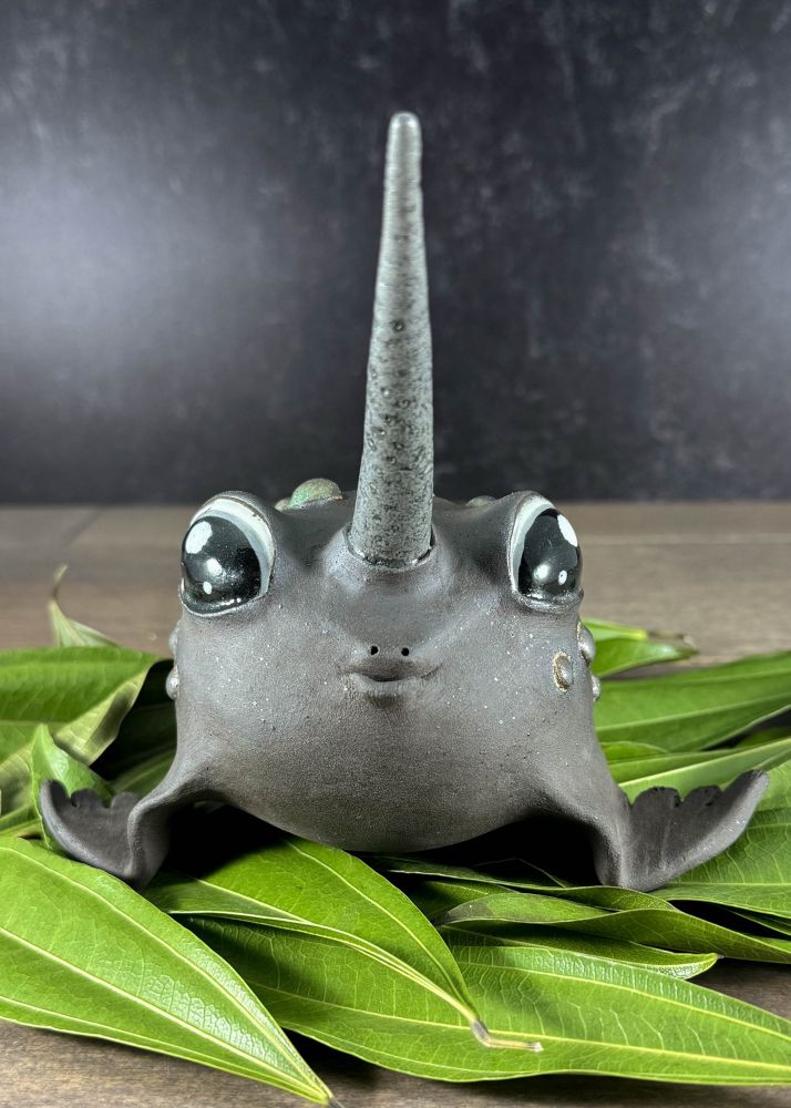 A mythical animal sculpture sits on a bed of leaves. It has big sweet eyes, a fish mouth, a narwhal horn, seal fins, toad spots, and a beaver tail all in dark clay. 

Meeble is an adult female rare Narwhal-Toad/Seal-Beaver mix up for adoption. She really loves kisses and will purse her fishy underbite for you day and night. However, she has no idea where her horn is most of the time and should always be supervised around small children and other animals. Meeble has been known to steal household items and use them to dam doorways, but her dams are artistic and comfortable, to be enjoyed by all. Adoption fee $245 plus transport costs. 