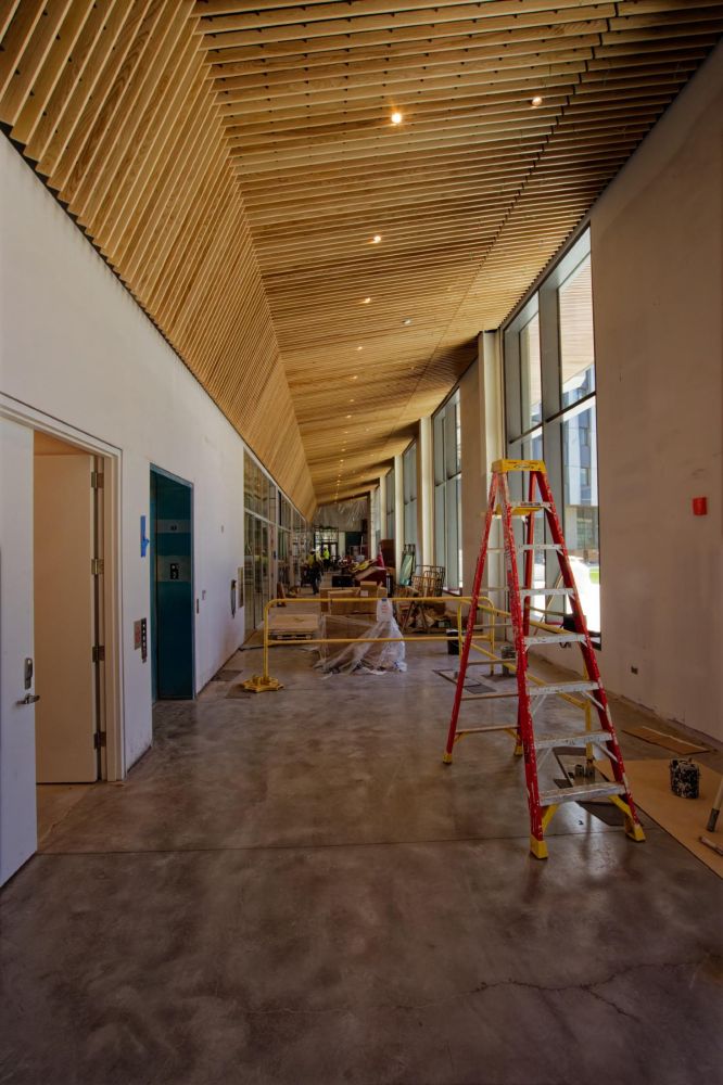 Equipment including ladders and barricades and workmen spread out in a new building with a bare concrete floor and a slanted ceiling (with two angles with doors to the left and windows to the right)