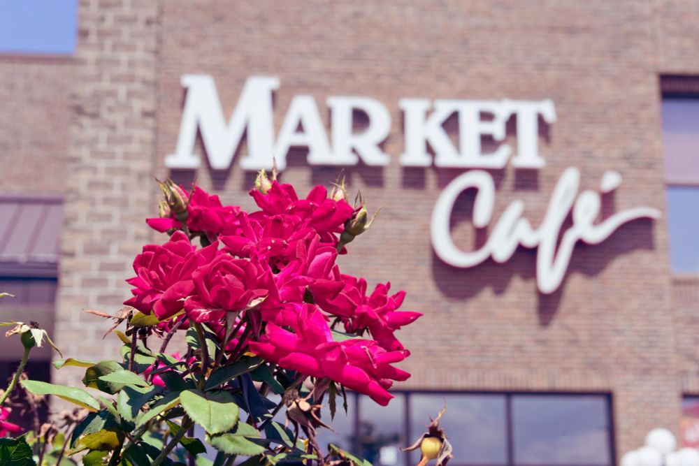 Cluster of Red Roses Rise Up from the Lower Left in front of a brick building with a sign that says MARKET Cafe.