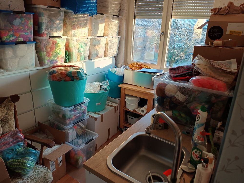 Room full of yarn in bins and boxes, kitchen counter full with boxes and a yarn bin