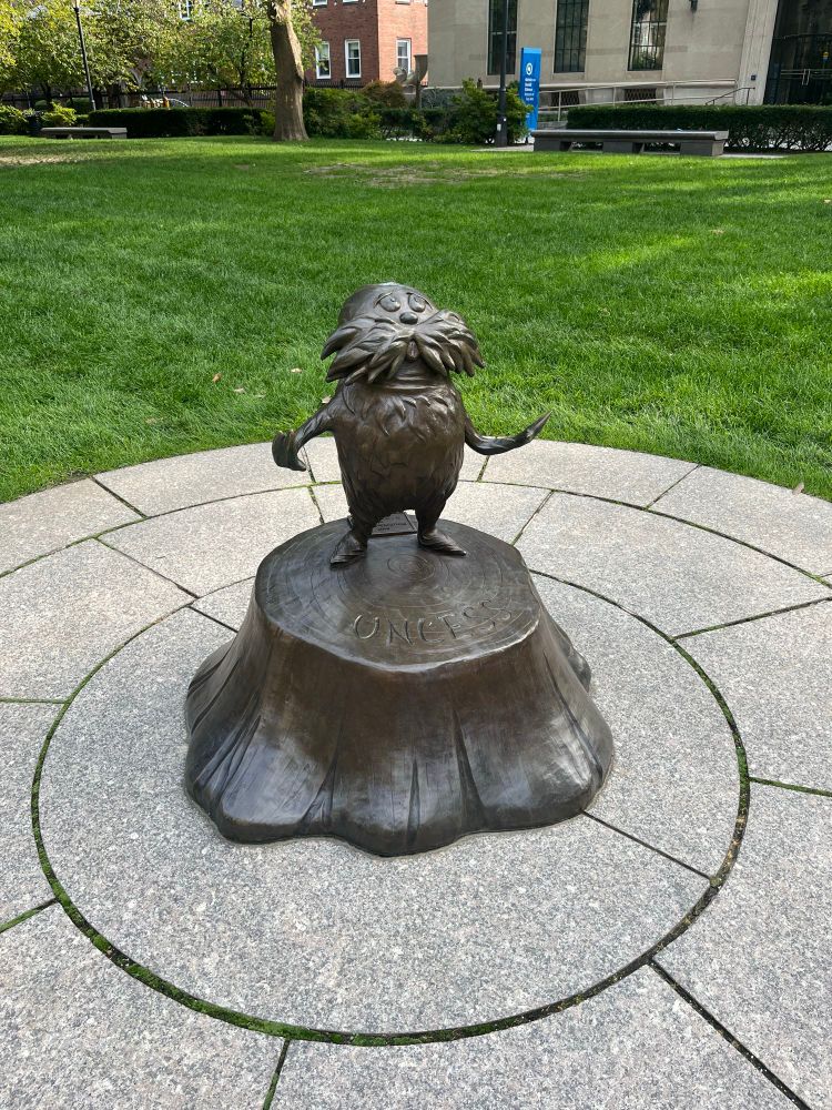A brown sculpture of the Lorax standing on a tree stump 